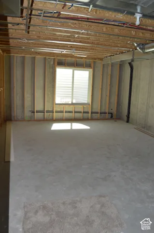 Unfinished interior space featuring exposed wood-stud framing, concrete flooring, and a single window with an external egress window well