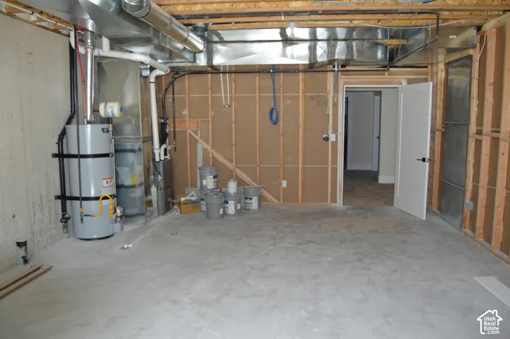 Unfinished utility space featuring exposed wood-stud wall framing, concrete foundation walls, and concrete flooring, housing an installed water heater and furnace system