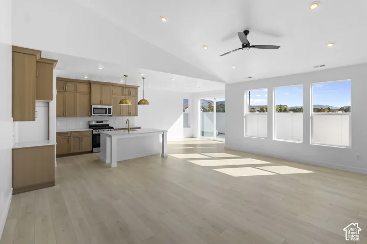 Open-concept living space featuring vaulted ceilings, recessed lighting, wood-finish flooring, a kitchen island with stone-surface countertops, and cabinetry with metal hardware