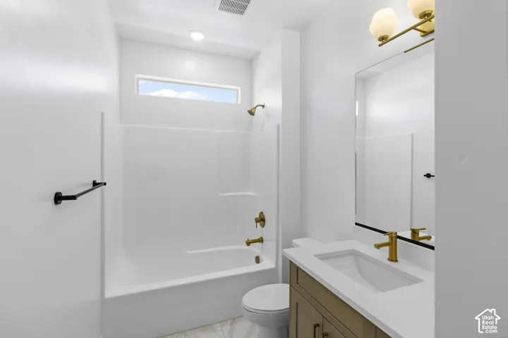 Bathroom featuring a vanity with a white countertop and gold-tone faucet, integrated tub and shower combination, transom window, and wall-mounted vanity lighting