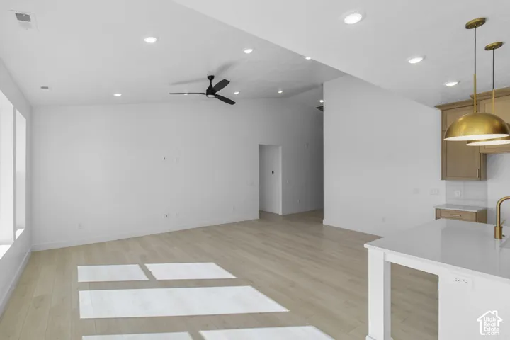 Open-concept interior featuring vaulted ceilings, light-toned wood-finish flooring, recessed lighting, and a kitchen island with stone-finish countertops and brass-tone pendant lighting
