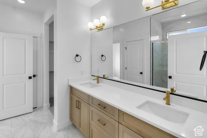 Dual-vanity bathroom featuring light wood-finish cabinetry, a white countertop with integrated sinks, brass-tone fixtures, and large-format tile flooring