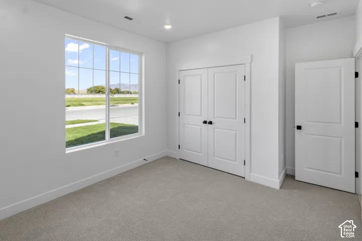 Neutral-toned carpeted flooring, white walls, recessed ceiling lighting, double-door closet with black hardware, and large window with mountain backdrop