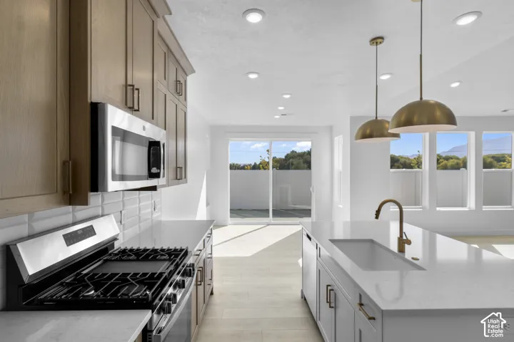 Kitchen featuring light-finish cabinetry, white countertops, a center island with a recessed sink, gold-tone hardware, and pendant lighting