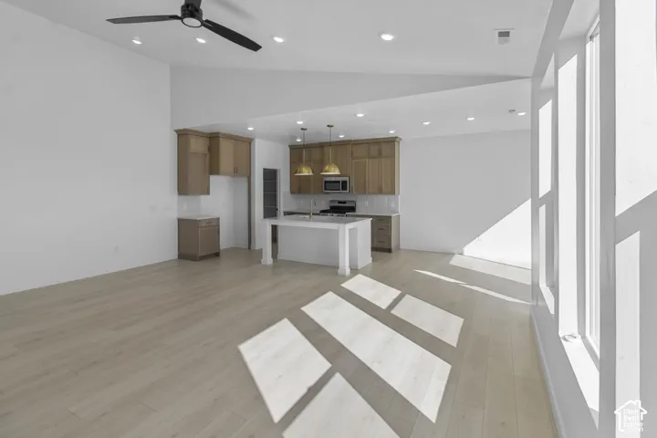 Open-concept interior featuring vaulted ceilings, wood-finish flooring, a center island with pendant lighting, and full-height windows