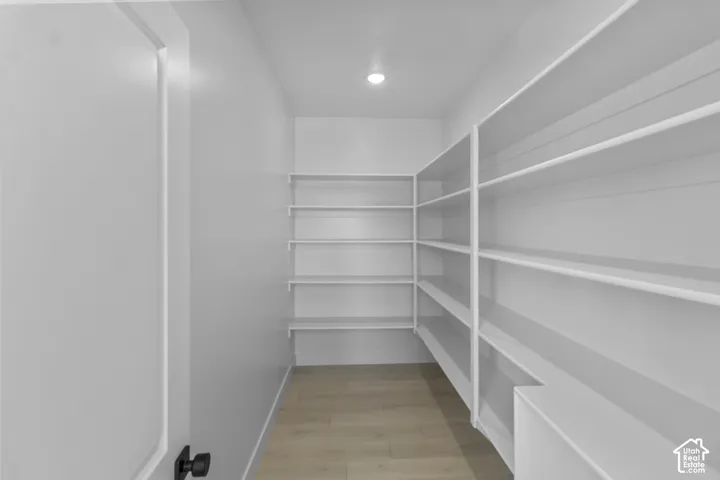 Walk-in storage featuring wrap-around white shelving, wood-finish flooring, and recessed ceiling lighting
