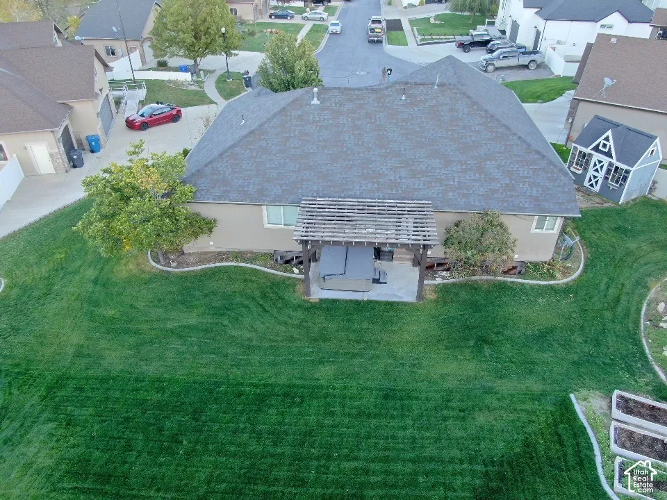 Rear exterior featuring a concrete patio, wood pergola, built-in hot tub, and expansive lawn with raised garden beds