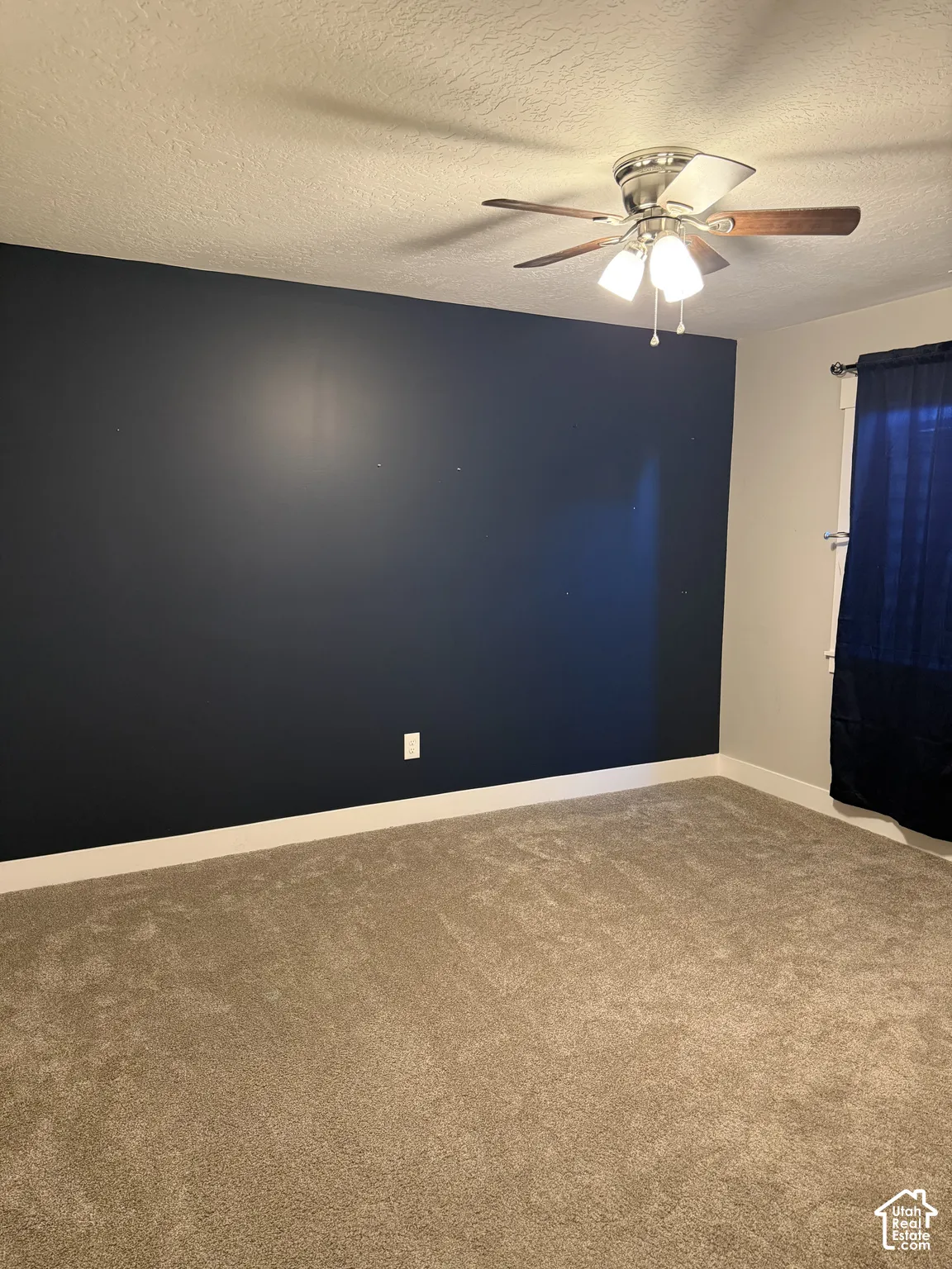 Room interior featuring a dark navy accent wall, neutral carpeting, and a multi-light ceiling fan with integrated wood-tone blades