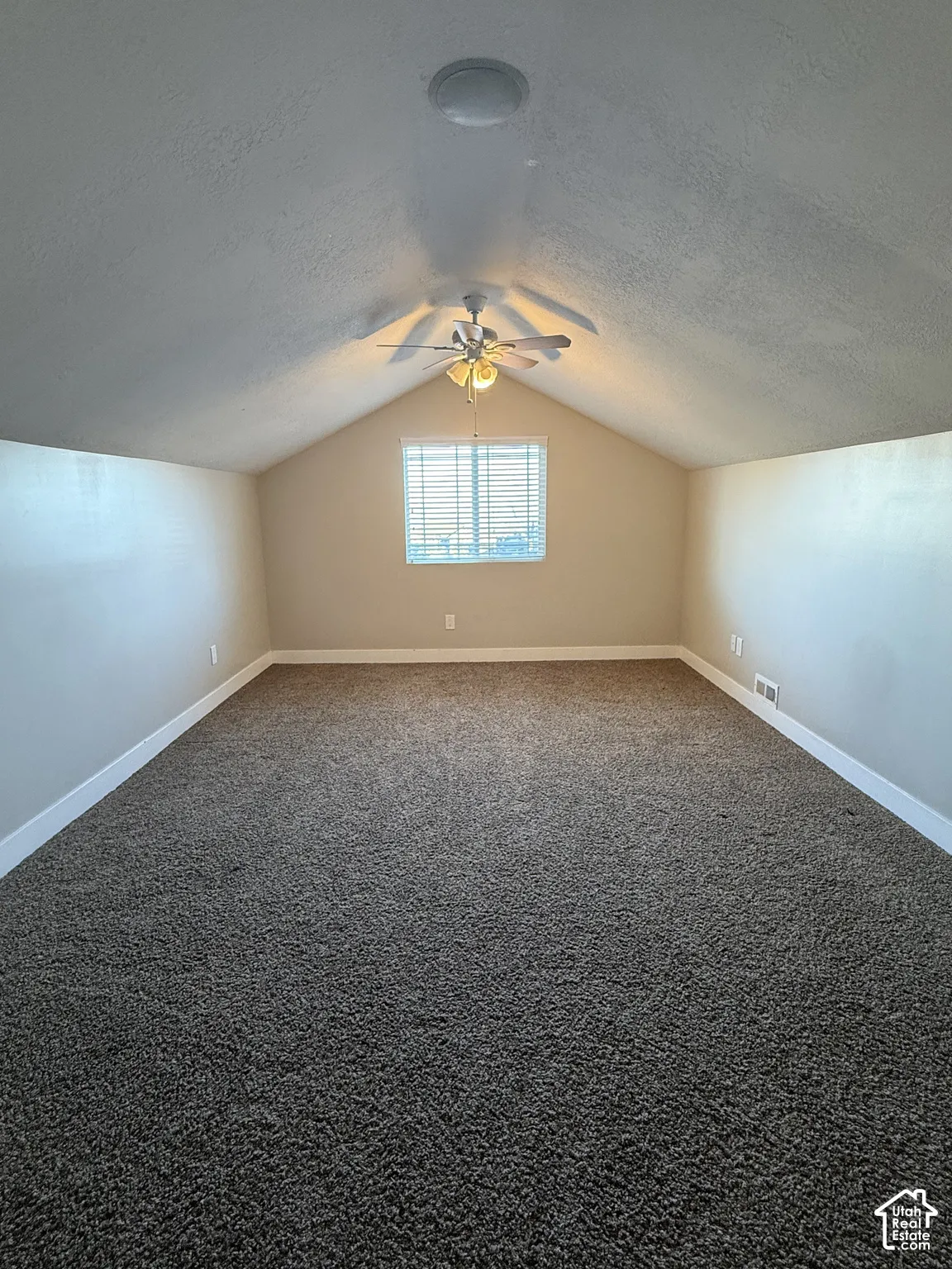 Vaulted ceiling featuring carpeted flooring, a center-mounted ceiling fan with integrated lighting, and a window with blinds