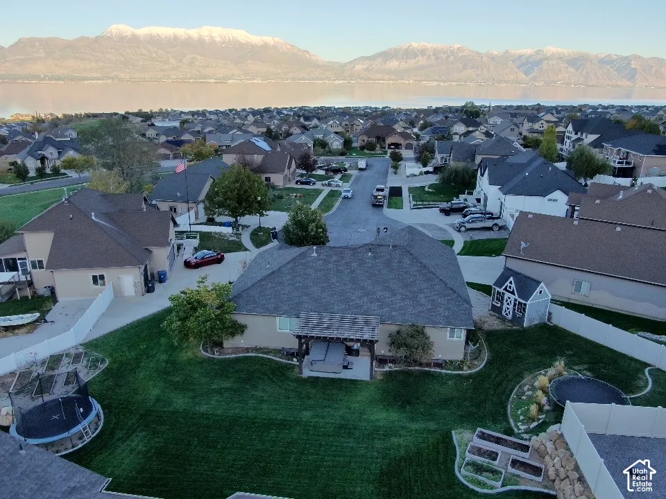 Aerial perspective showcasing a landscaped backyard with a covered patio, garden beds, and mountain scenery
