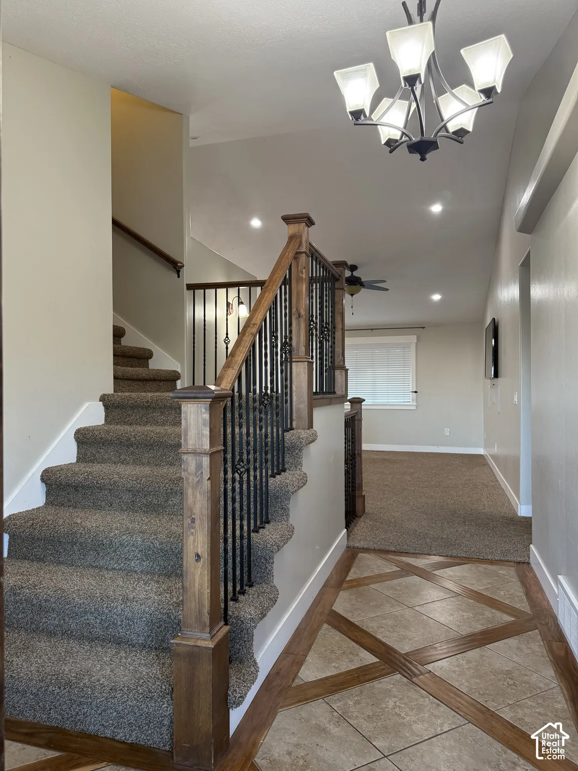 Entryway featuring patterned tile and wood-inlay flooring, a multi-arm chandelier, and a staircase with stained wood newel posts and metal balusters