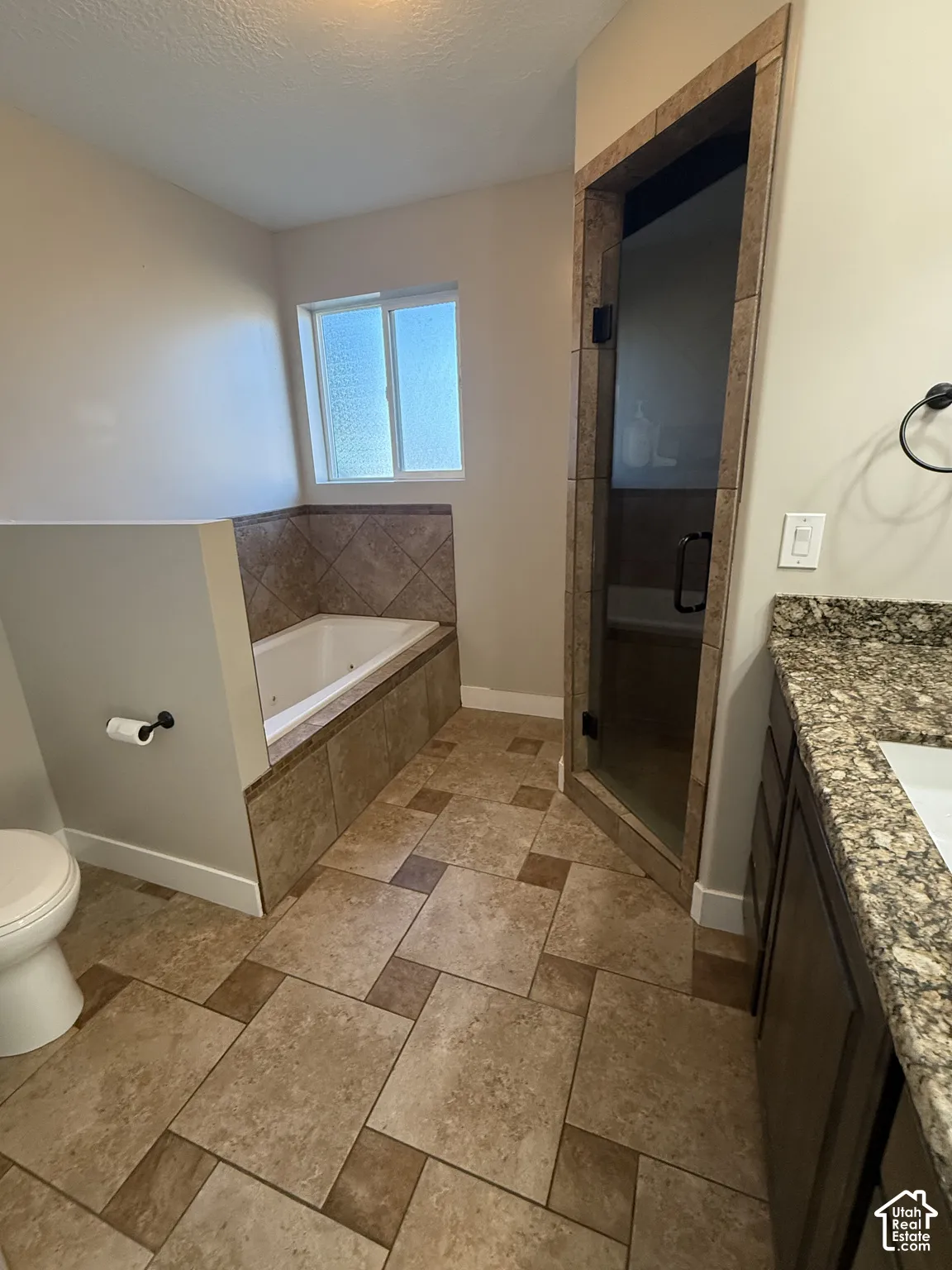Bathroom featuring a built-in soaking tub with tile surround, a glass-enclosed shower, stone-finish vanity countertop, and multi-tone floor tiling