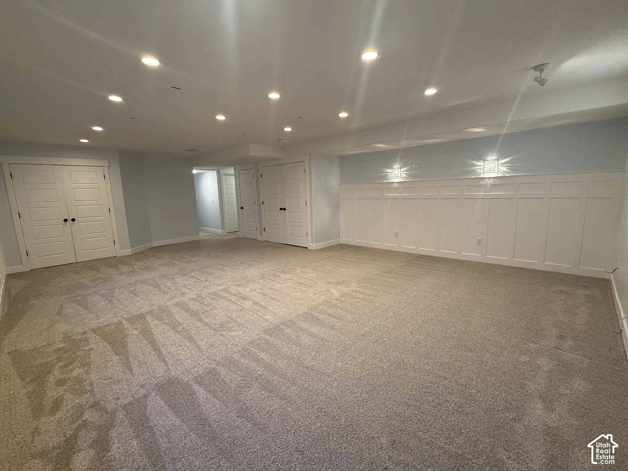 Spacious room featuring wall-to-wall carpeting, recessed ceiling lighting, extensive white wainscoting, and multiple sets of double-panel doors