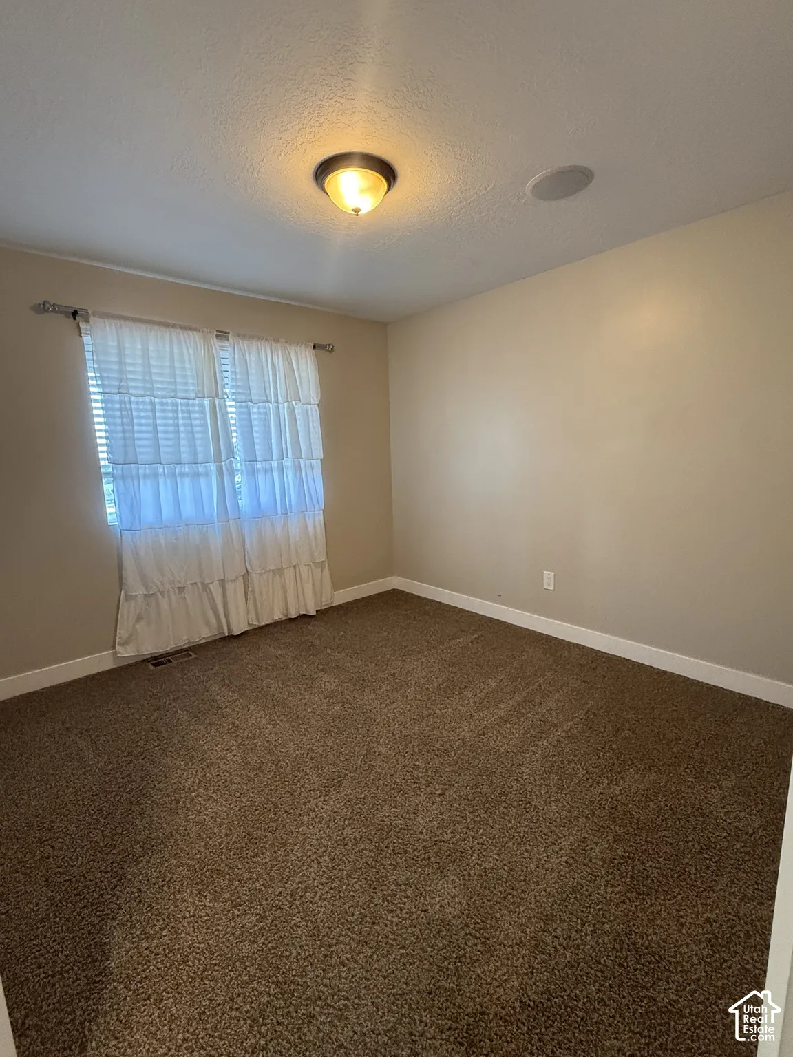 Neutral interior space featuring wall-to-wall carpeting, a flush-mount ceiling light fixture, and an integrated ceiling speaker