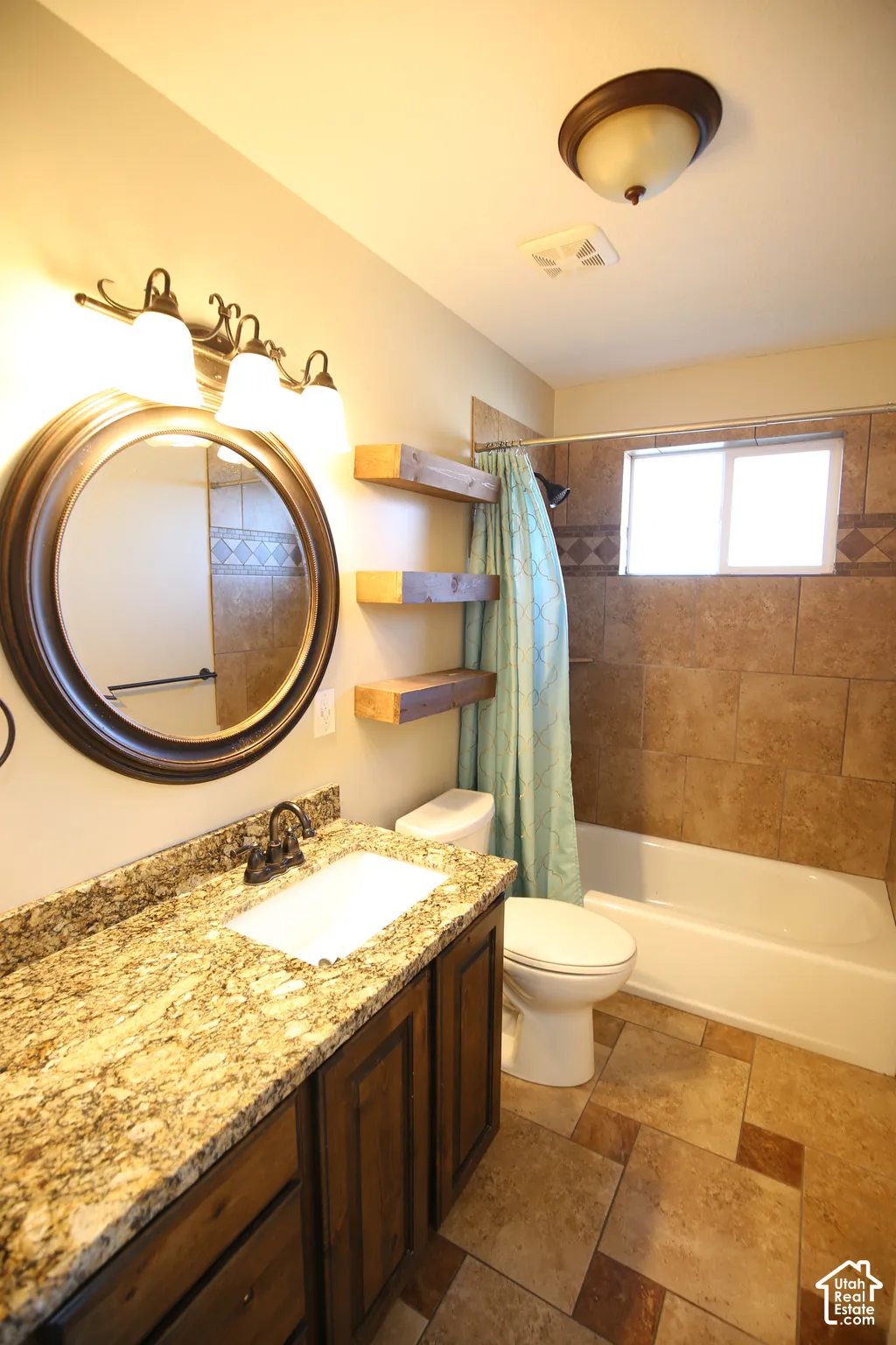 Bathroom featuring a vanity with stone-finish countertop, under-mount sink, oil-rubbed bronze fixtures, floating wood shelving, and tiled tub surround