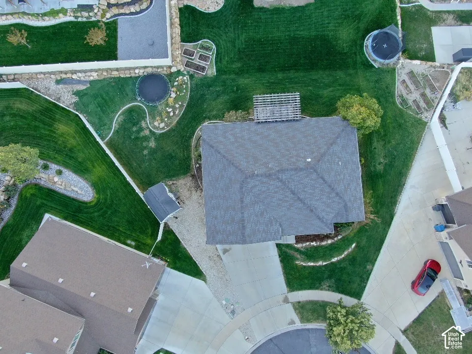 Aerial perspective of the lot featuring a sprawling lawn, structured rock-lined landscaping, a built-in pergola, and a dedicated storage shed