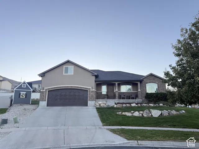 Exterior featuring a stucco and brick facade, covered entryway, attached garage, and stone-retaining wall landscaping