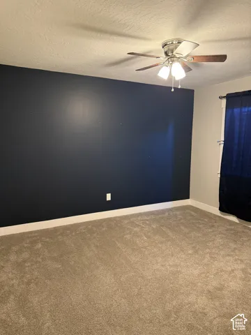 Room interior featuring a dark navy accent wall, neutral carpeting, and a multi-light ceiling fan with integrated wood-tone blades