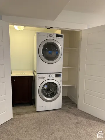 Laundry closet featuring stacked front-load appliances, a dark wood-finish vanity with an integrated sink, built-in shelving, and neutral wall-to-wall carpeting