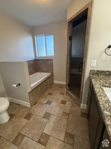Bathroom featuring a built-in soaking tub with tile surround, a glass-enclosed shower, stone-finish vanity countertop, and multi-tone floor tiling