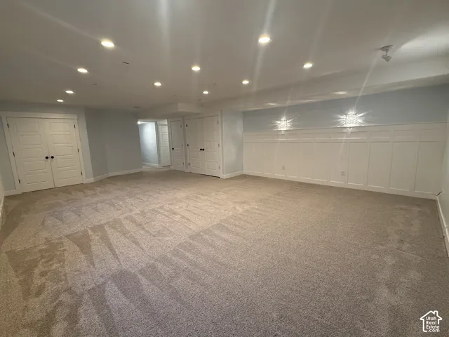 Spacious room featuring wall-to-wall carpeting, recessed ceiling lighting, extensive white wainscoting, and multiple sets of double-panel doors