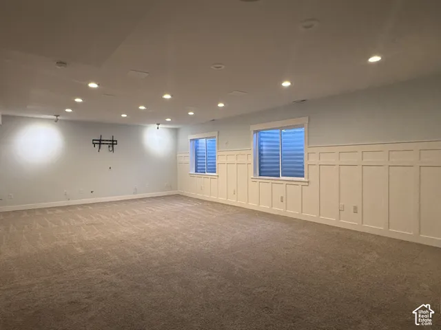 Expansive interior space featuring neutral wall-to-wall carpeting, white grid wainscoting, recessed lighting, and two egress windows