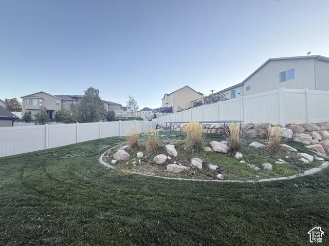 Backyard featuring a manicured lawn, tiered stone retaining walls, ornamental grasses, and white vinyl privacy fencing