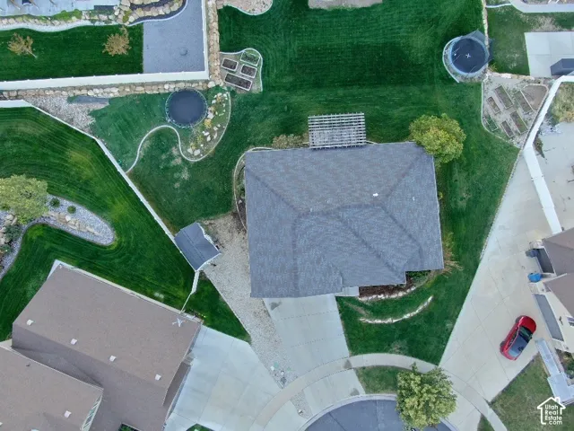 Aerial perspective of the lot featuring a sprawling lawn, structured rock-lined landscaping, a built-in pergola, and a dedicated storage shed
