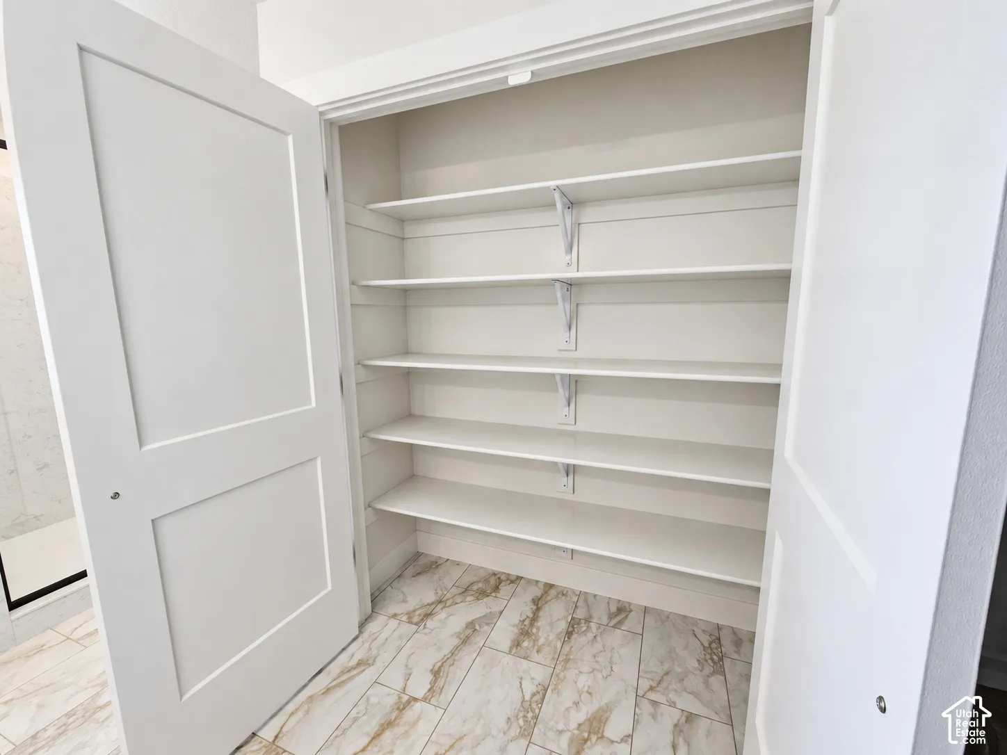 Storage space featuring five tiers of white shelving, plank-style stone-finish flooring, and double panel doors