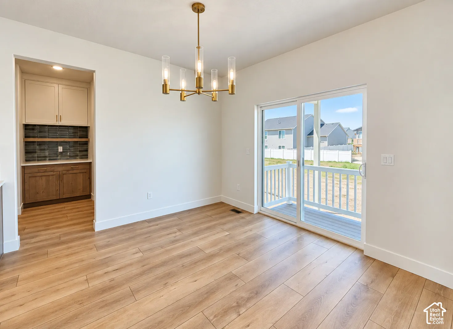 Wood-finish flooring, brass-finish multi-light chandelier, sliding glass door with exterior deck access, and built-in cabinetry with tiled backsplash