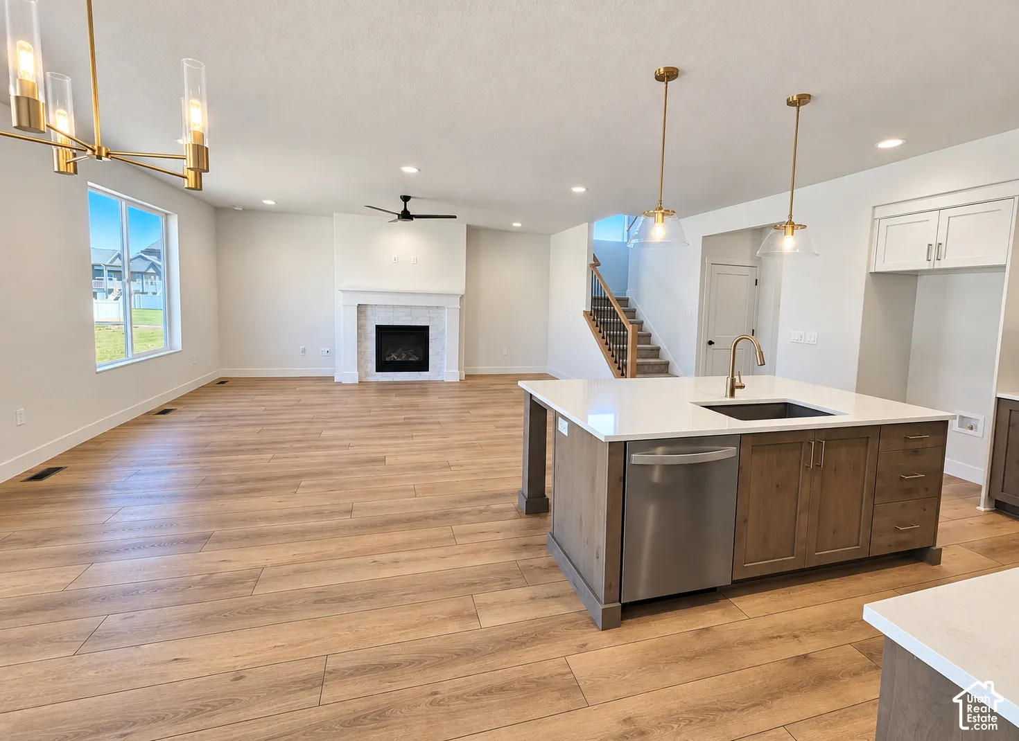 Open-concept interior featuring wood-finish flooring, a kitchen island with stone countertops and stainless-steel appliances, a fireplace with a decorative tile surround, and modern pendant lighting