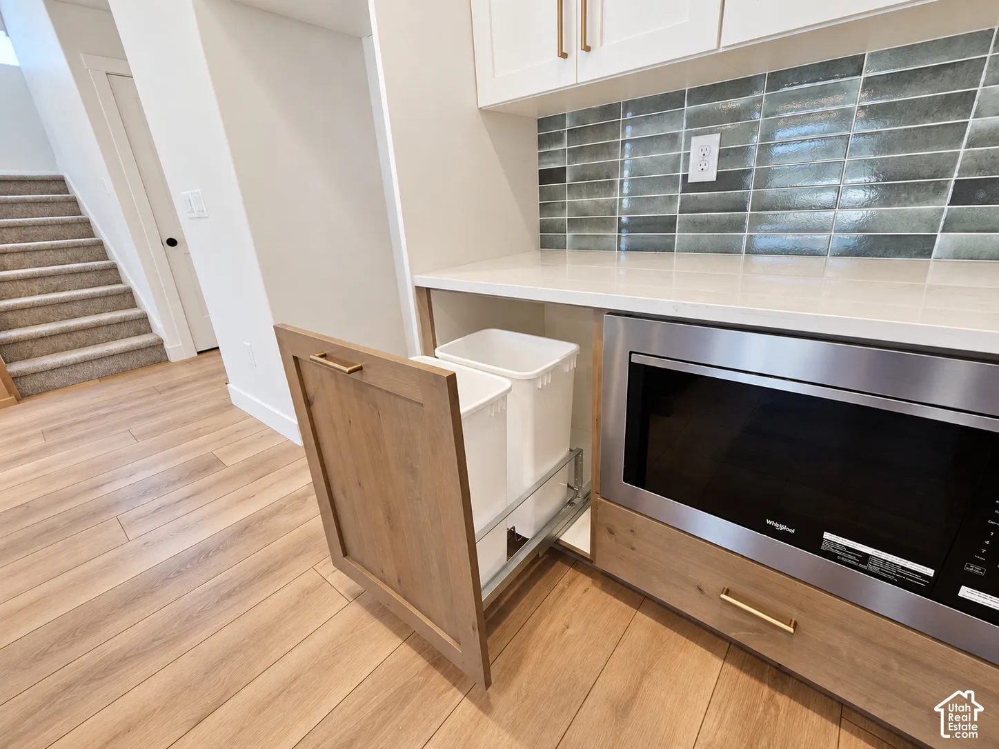 Kitchen cabinetry featuring a built-in slide-out waste bin, quartz countertop, stacked tile backsplash, and integrated stainless steel microwave