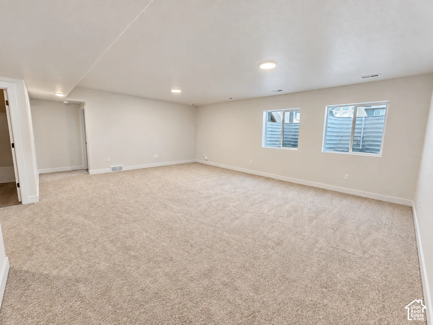 Open-concept interior featuring neutral wall paint, wall-to-wall carpeting, recessed ceiling lighting, and two egress windows with metal window wells