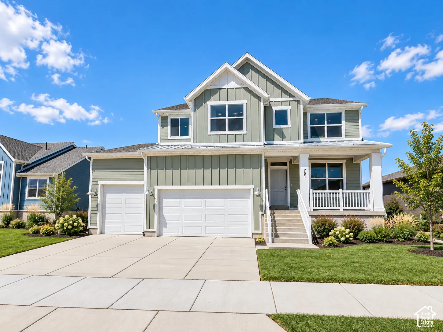 Two-story residence featuring vertical siding, a covered front porch with white railing, a three-car garage, and concrete driveway
