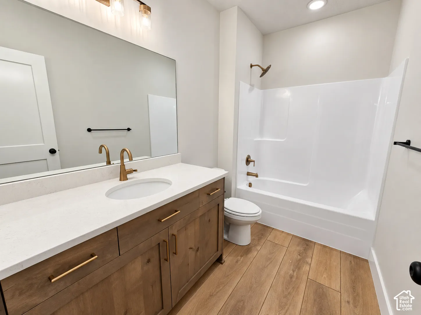 Bathroom featuring wood-finish cabinetry, white countertop with an integrated basin, wood-finish flooring, and metallic hardware fixtures