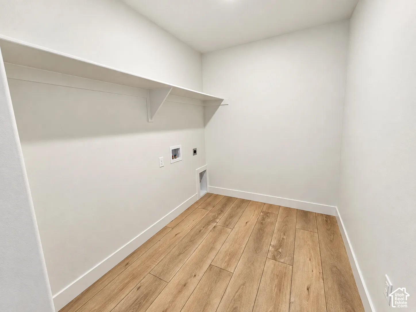 Utility space featuring wood-finish flooring, a wall-mounted shelf, and recessed laundry hookups
