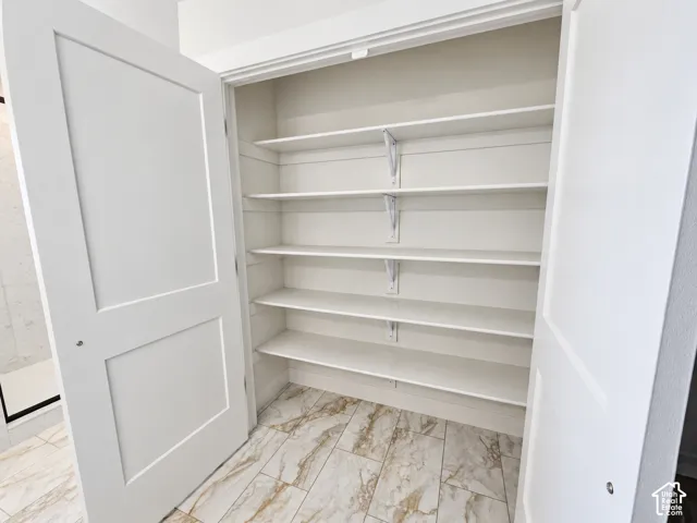 Storage space featuring five tiers of white shelving, plank-style stone-finish flooring, and double panel doors