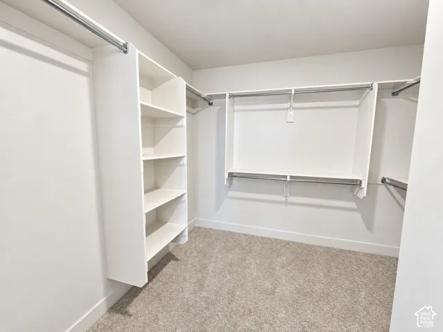 Walk-in closet featuring white tiered shelving, dual-level metal garment rods, and wall-to-wall carpeting
