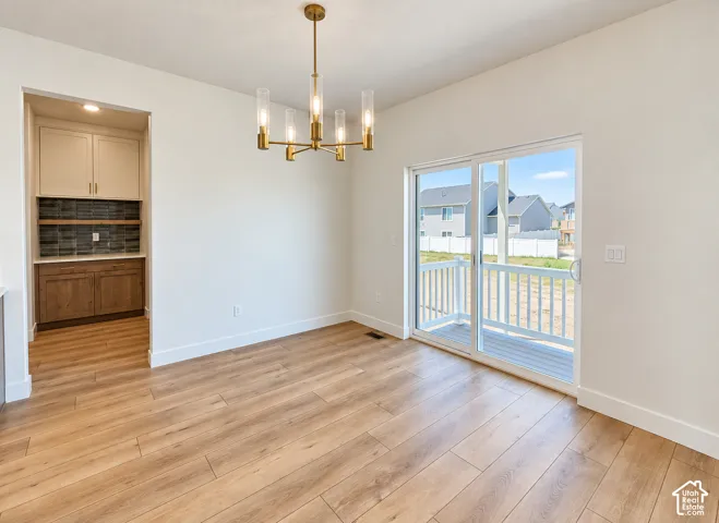 Wood-finish flooring, brass-finish multi-light chandelier, sliding glass door with exterior deck access, and built-in cabinetry with tiled backsplash