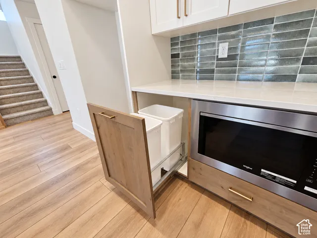 Kitchen cabinetry featuring a built-in slide-out waste bin, quartz countertop, stacked tile backsplash, and integrated stainless steel microwave