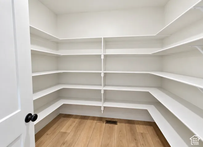 Walk-in storage space featuring multi-level wrap-around shelving and wood-finish flooring