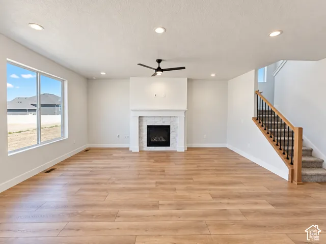 Living area featuring wood-finish flooring, a central fireplace with stone-surround, recessed lighting, a modern ceiling fan, and a staircase with a wooden handrail and black metal balusters