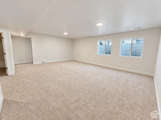 Open-concept interior featuring neutral wall paint, wall-to-wall carpeting, recessed ceiling lighting, and two egress windows with metal window wells