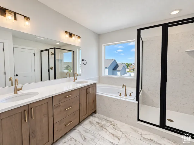 Dual-sink vanity with light wood-finish cabinetry, quartz countertops, soaking tub, and separate walk-in shower with matte black fixtures
