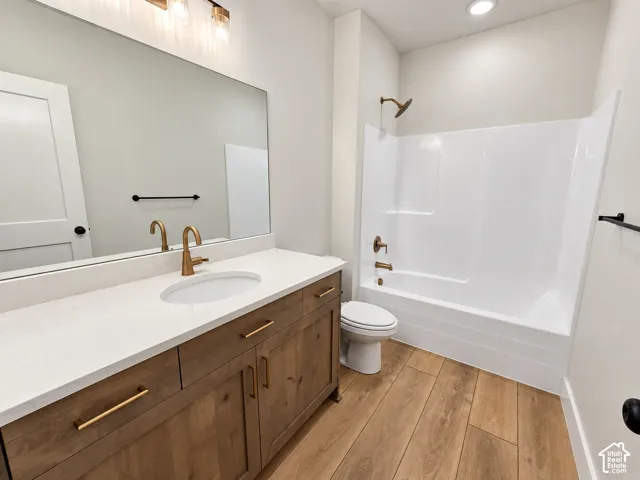Bathroom featuring wood-finish cabinetry, white countertop with an integrated basin, wood-finish flooring, and metallic hardware fixtures