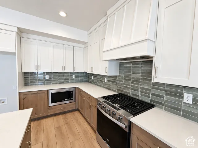 Kitchen featuring shaker-style upper cabinetry with a custom vent hood, lower wood-finish cabinetry, quartz countertops, a subway tile backsplash, and stainless steel gas range
