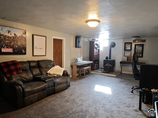 Interior space featuring a white painted brick hearth, a cast-iron wood-burning stove, wall-to-wall carpeting, and flush-mount ceiling lighting