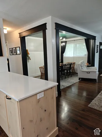 Kitchen island with white quartz countertop and light-finish wood cabinetry, complemented by dark-stained interior doorway trim and wood-finish flooring