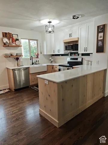 Kitchen featuring white upper cabinetry, natural wood-finish lower cabinetry, white quartz countertops, a farmhouse-style apron sink with a matte black faucet, and wood-finish flooring