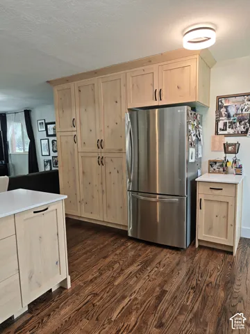 Light-toned wood cabinetry featuring matte black hardware, stainless steel refrigerator, white countertops, wood-finish flooring, and circular LED flush-mount lighting